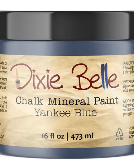 A jar of Dixie Belle Chalk Mineral Paint in the color Yankee Blue, featuring a black lid and a tan paper label with dark blue-gray plastic jar body.