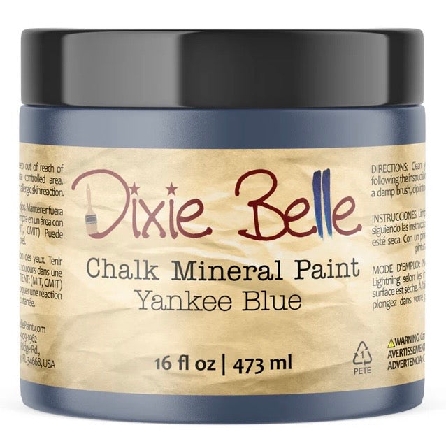 A jar of Dixie Belle Chalk Mineral Paint in the color Yankee Blue, featuring a black lid and a tan paper label with dark blue-gray plastic jar body.