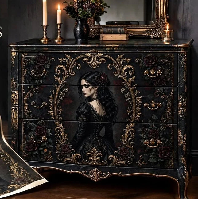A dark, ornate Gothic-style wooden dresser or chest with three drawers, decorated with intricate gold filigree, red roses, and a painted portrait of a woman in a black dress on the front. The dresser is styled in a moody room setting with candles, books, and a mirror on top.