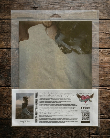 A packaged sheet of decoupage paper displayed on a rustic dark wood background. The clear plastic sleeve contains a printed sheet with a painted illustration of a woman's face and neck, plus a white instruction label at the bottom with text, a small example photo, and the brand name Whimsykel Designs
