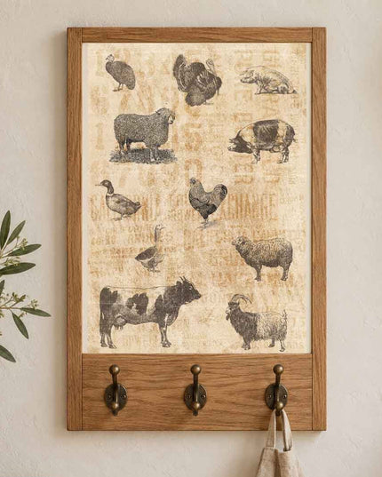 A framed rustic wall art piece with animal sketches hangs on a white wall above a wooden hook rack with three dark metal hooks. The artwork is Redesign with Prima decoupage paper Barnyard Sketches and features sheep, chickens, a pig, duck, cow, and goat illustrations on a textured cream background, and the frame and lower rack are made of medium brown wood.